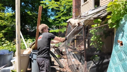 Worker removing an old metal frame structure and mattress from a backyard